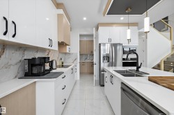 Modern kitchen featuring white and wood-finish cabinetry, quartz countertops, a stone-look backsplash, and integrated stainless steel appliances - 