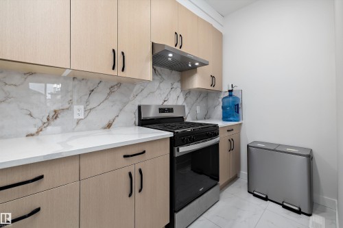 Kitchen featuring light wood-finish cabinetry with black hardware, white countertops, and a white and brown veined backsplash - 403 Pine Point, Leduc, AB 