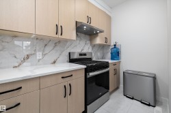 Kitchen featuring light wood-finish cabinetry with black hardware, white countertops, and a white and brown veined backsplash - 
