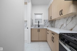 Modern galley kitchen featuring light wood-finish cabinetry with black hardware, white countertops, and a full-height veined backsplash - 