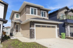 Two-story residence featuring a neutral-toned siding facade, stone veneer accents, and an integrated garage with an overhead door - 