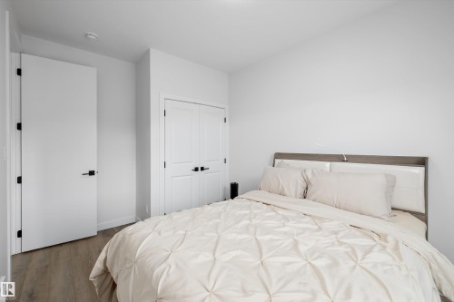 Neutral bedroom featuring wood-finish flooring, a double-door closet with black hardware, and a single entry door with matching black hardware - 403 Pine Point, Leduc, AB 