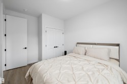 Neutral bedroom featuring wood-finish flooring, a double-door closet with black hardware, and a single entry door with matching black hardware - 