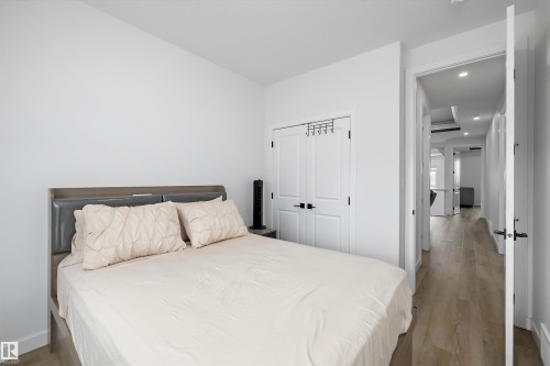 White walls, wood-finish flooring, and white bi-fold closet doors with black hardware - 403 Pine Point, Leduc, AB 