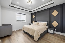 Bedroom featuring a decorative accent wall with geometric paneling, tray ceiling with recessed lighting, central flush-mount fixture, wood-finish flooring, and a large window - 