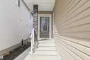 Front entrance featuring a brown door with clear glass panels, concrete steps, and a white handrail - 403 Pine Point, Leduc, AB 
