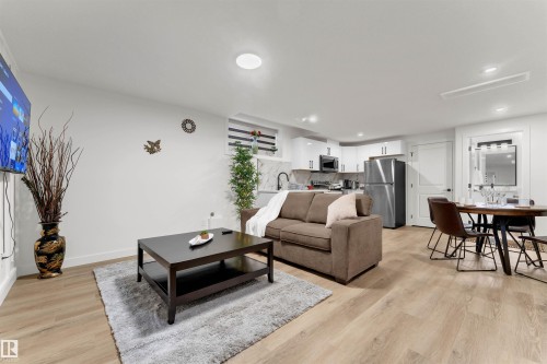 Open concept living space featuring wood-finish flooring, recessed lighting, and a modern kitchen with white cabinetry and stainless steel appliances - 403 Pine Point, Leduc, AB 