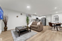 Open concept living space featuring wood-finish flooring, recessed lighting, and a modern kitchen with white cabinetry and stainless steel appliances - 