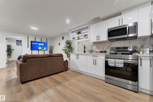 Modern kitchen featuring white high-gloss cabinetry, stainless steel appliances, and a marble-patterned backsplash - 403 Pine Point, Leduc, AB 