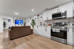 Modern kitchen featuring white high-gloss cabinetry, stainless steel appliances, and a marble-patterned backsplash - 