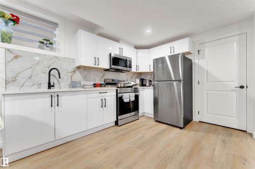 Modern kitchen featuring white cabinetry, a stainless steel appliance suite, marble-look slab backsplash, and wood-finish flooring - 403 Pine Point, Leduc, AB 