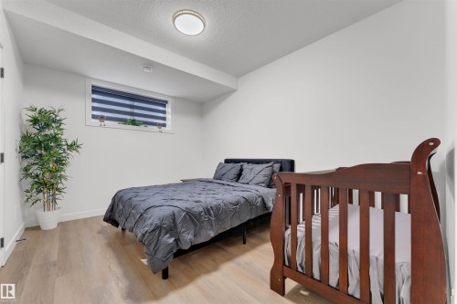 Spacious room featuring light wood-finish flooring, a contemporary flush-mount ceiling light, a transom window with horizontal blinds, and clean white walls - 403 Pine Point, Leduc, AB 