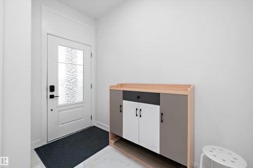 Entryway featuring a white paneled door with decorative glass, modern black hardware, and a transom window above - 403 Pine Point, Leduc, AB 