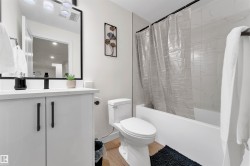 Bathroom featuring a white vanity with matte black hardware, a black-framed mirror, and a full bathtub with white tile surround - 