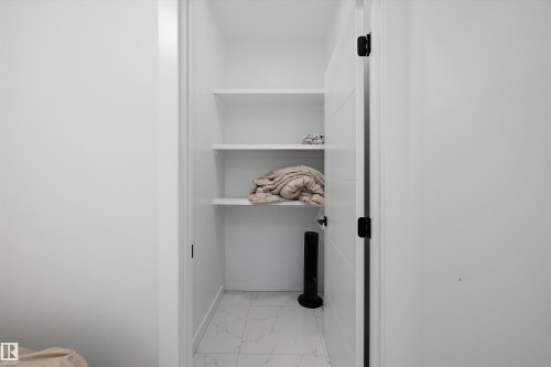 Recessed storage area featuring white shelving, white walls, and light-toned tile flooring with subtle veining - 403 Pine Point, Leduc, AB 