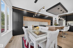 Modern kitchen featuring black and wood-finish cabinetry, an oversized island with seating, stainless steel appliances, and wood-finish flooring - 