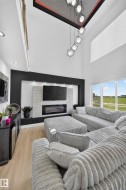 Vaulted ceiling with a geometric chandelier, integrated entertainment wall with an electric fireplace, wood-finish flooring, and large windows - 