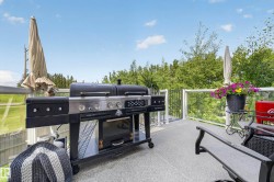 Expansive outdoor deck featuring a textured surface, clear glass railings, and multiple shade umbrellas - 