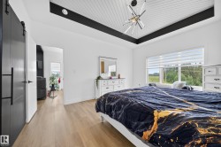 Room featuring wood-finish flooring, a white tray ceiling with black beams and white tongue-and-groove paneling, and a modern ceiling light fixture - 