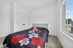 Bedroom featuring a large window, light-toned carpet flooring, white walls, and a closet with double doors and black hardware - 