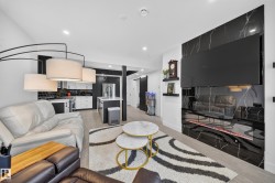 Open-concept living space featuring a black marble-finish accent wall with integrated media console, an electric fireplace, wood-finish flooring, and recessed lighting - 