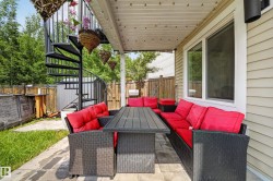 Covered patio area featuring a spiral staircase, stone paver flooring, and beige horizontal siding - 