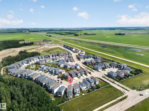 Aerial perspective showcasing a residential community with contemporary homes, bordered by expansive green fields and a distant highway - 626 Astoria Way, Devon, AB 