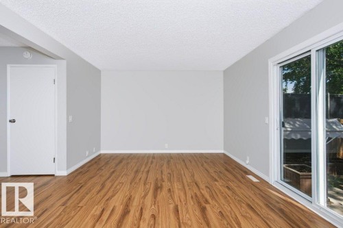 Spacious room featuring light gray walls, wood-finish flooring, and white baseboards - 24 14511 52 Street, Edmonton, AB 