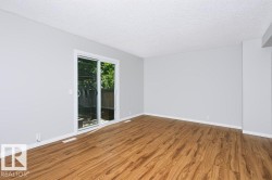 Spacious room featuring wood-finish flooring, light grey walls, and a white sliding glass door providing outdoor access - 