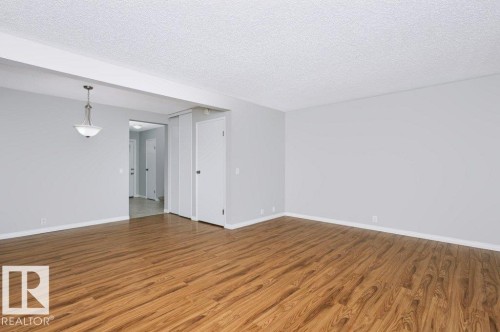 Expansive room featuring wood-finish flooring, light gray wall paint, white trim, and a textured ceiling - 24 14511 52 Street, Edmonton, AB 