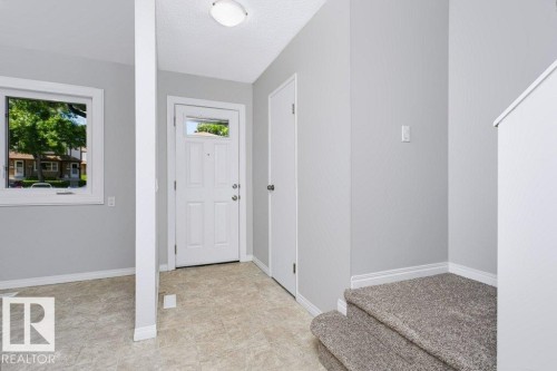 Entryway featuring a paneled door with transom window, light gray walls, and textured flooring - 24 14511 52 Street, Edmonton, AB 