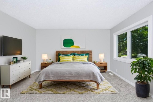 Carpeted room featuring a wood-finish bed frame with a headboard, two integrated nightstands, and a large window with white trim - 24 14511 52 Street, Edmonton, AB 
