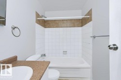 Bathroom featuring a white bathtub, white tiled shower surround with a brown accent band, a toilet, a vanity with a speckled countertop, and a recessed medicine cabinet - 
