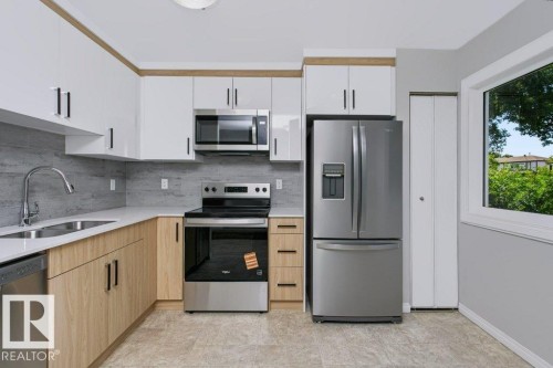 Contemporary kitchen featuring white upper cabinetry, wood-finish lower cabinetry, and stainless steel appliances - 24 14511 52 Street, Edmonton, AB 