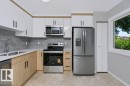 Contemporary kitchen featuring white upper cabinetry, wood-finish lower cabinetry, and stainless steel appliances - 24 14511 52 Street, Edmonton, AB 