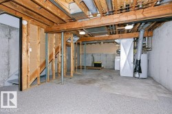 Unfinished basement featuring exposed wood joists, concrete foundation walls, and a partial subfloor - 