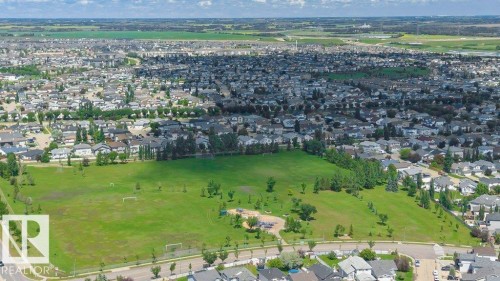 Expansive green space featuring a large grassy field, mature trees, and a visible playground structure - 24 14511 52 Street, Edmonton, AB 