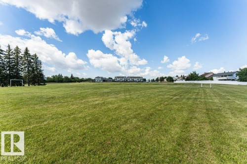 Expansive green space featuring a manicured lawn, distant residential structures, and mature evergreen trees - 24 14511 52 Street, Edmonton, AB 