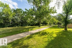 Expansive green space featuring a paved pathway, mature trees, and natural landscaping - 