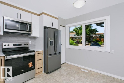 Modern kitchen featuring stainless steel appliances, white and wood-finish cabinetry, light grey countertops, and a subway tile backsplash - 24 14511 52 Street, Edmonton, AB 