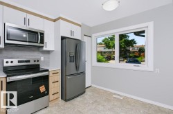 Modern kitchen featuring stainless steel appliances, white and wood-finish cabinetry, light grey countertops, and a subway tile backsplash - 
