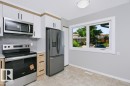 Modern kitchen featuring stainless steel appliances, white and wood-finish cabinetry, light grey countertops, and a subway tile backsplash - 24 14511 52 Street, Edmonton, AB 