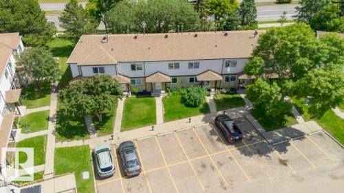 Multi-unit residential building with light-colored siding, brown roofing, individual front entrances, and an adjacent paved parking area - 24 14511 52 Street, Edmonton, AB 