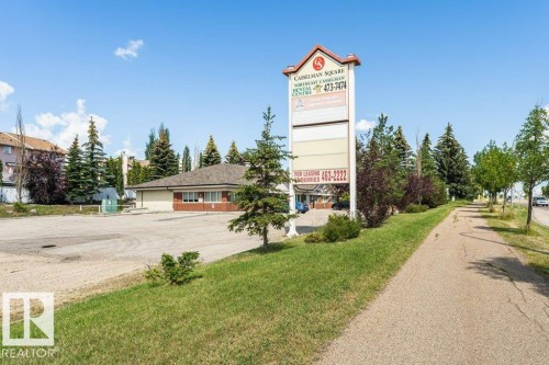 Commercial property featuring a prominent pylon sign with multiple panels, a building with a brown shingle roof, brick accents, and a large paved parking area - 24 14511 52 Street, Edmonton, AB 