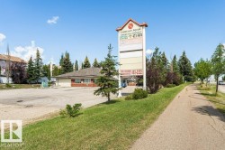 Commercial property featuring a prominent pylon sign with multiple panels, a building with a brown shingle roof, brick accents, and a large paved parking area - 