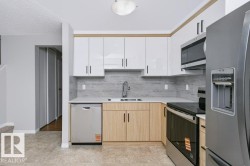 Modern kitchen featuring two-tone cabinetry with white upper and wood-finish lower cabinets, stainless steel appliances, light-colored countertops, and a full-height tile backsplash - 