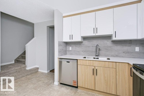 Contemporary kitchen featuring white upper cabinetry, wood-finish lower cabinetry, and stainless steel appliances - 24 14511 52 Street, Edmonton, AB 