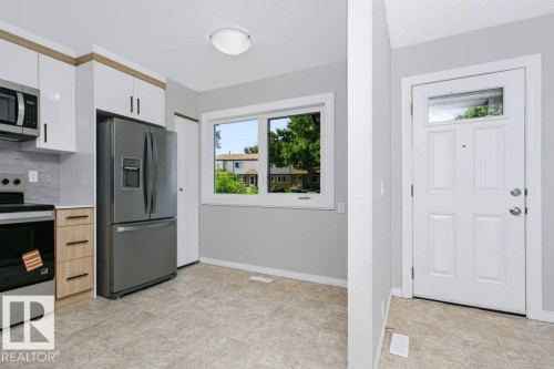 Modern kitchen featuring stainless steel appliances, white flat-panel upper cabinetry, wood-finish lower cabinetry, and a grey tile backsplash - 24 14511 52 Street, Edmonton, AB 