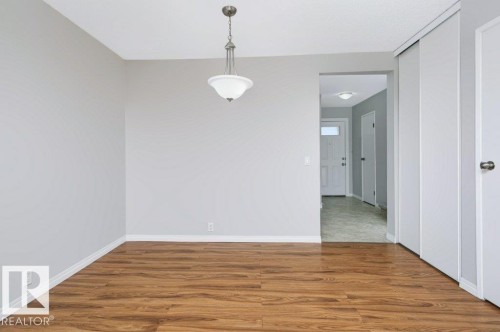 Spacious room featuring wood-finish flooring, light grey painted walls, white baseboards, and a ceiling-mounted pendant light fixture - 24 14511 52 Street, Edmonton, AB 