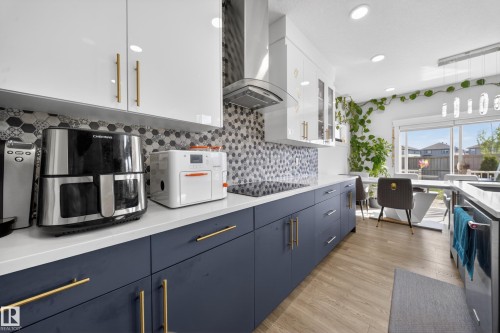 Modern kitchen featuring two-tone cabinetry with gold-finish hardware, light wood-finish flooring, a patterned tile backsplash, and an integrated cooktop - 1927 18 Street, Edmonton, AB 